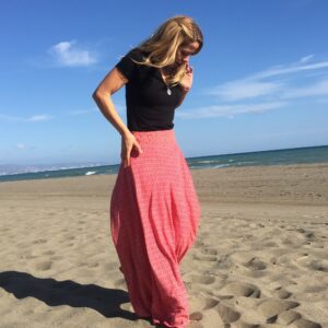 mujer de perfil con una falda larga estampada color pink caminando en la playa