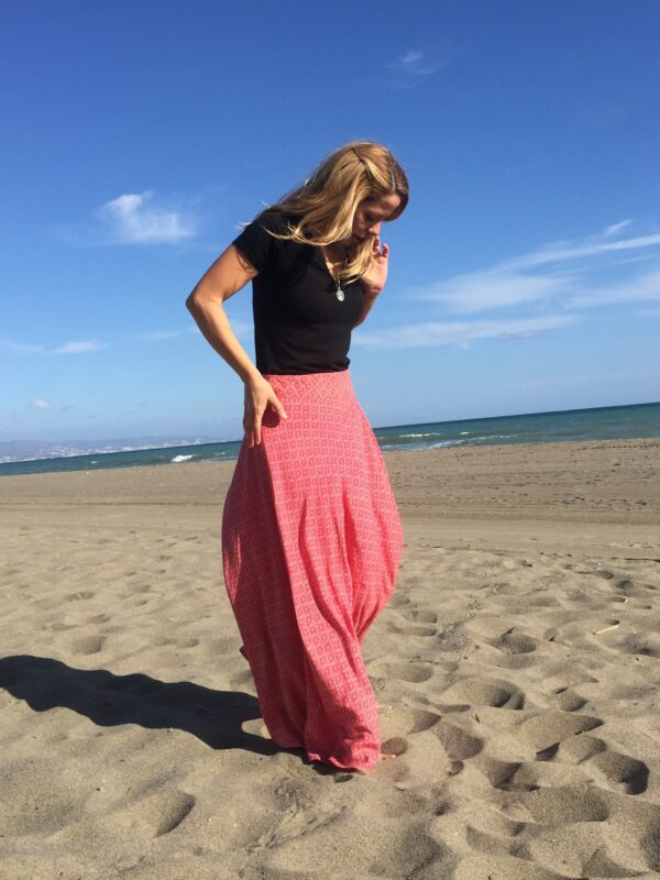 mujer de perfil con una falda larga estampada color pink caminando en la playa