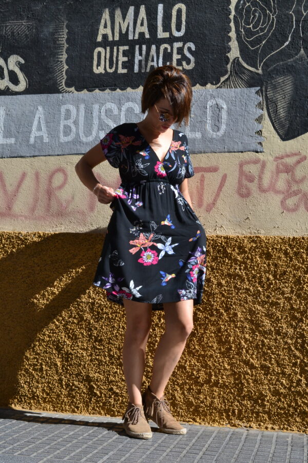 mujer en vestido estampado delante de un muro con las manos en los bolsillos